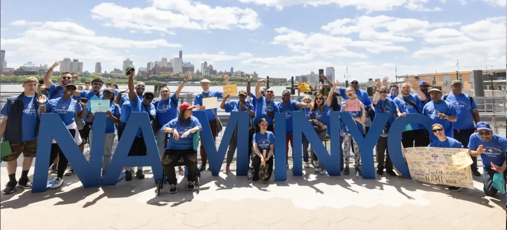 A group of people wearing blue shirts standing with letters saying NAMI NYC.