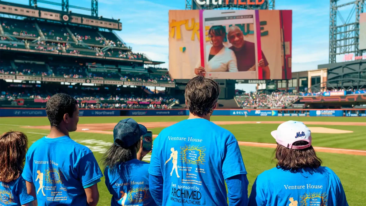 Venture House members on a professional baseball field in matching shirts with their backs to the camera