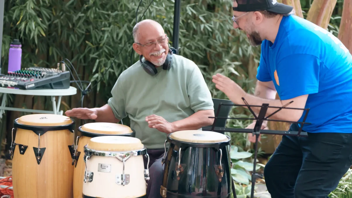 A man playing drums with someone cheering him on.